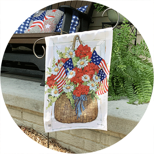 A garden flag showing a red, white and blue flower arrangement in a wicker basket.